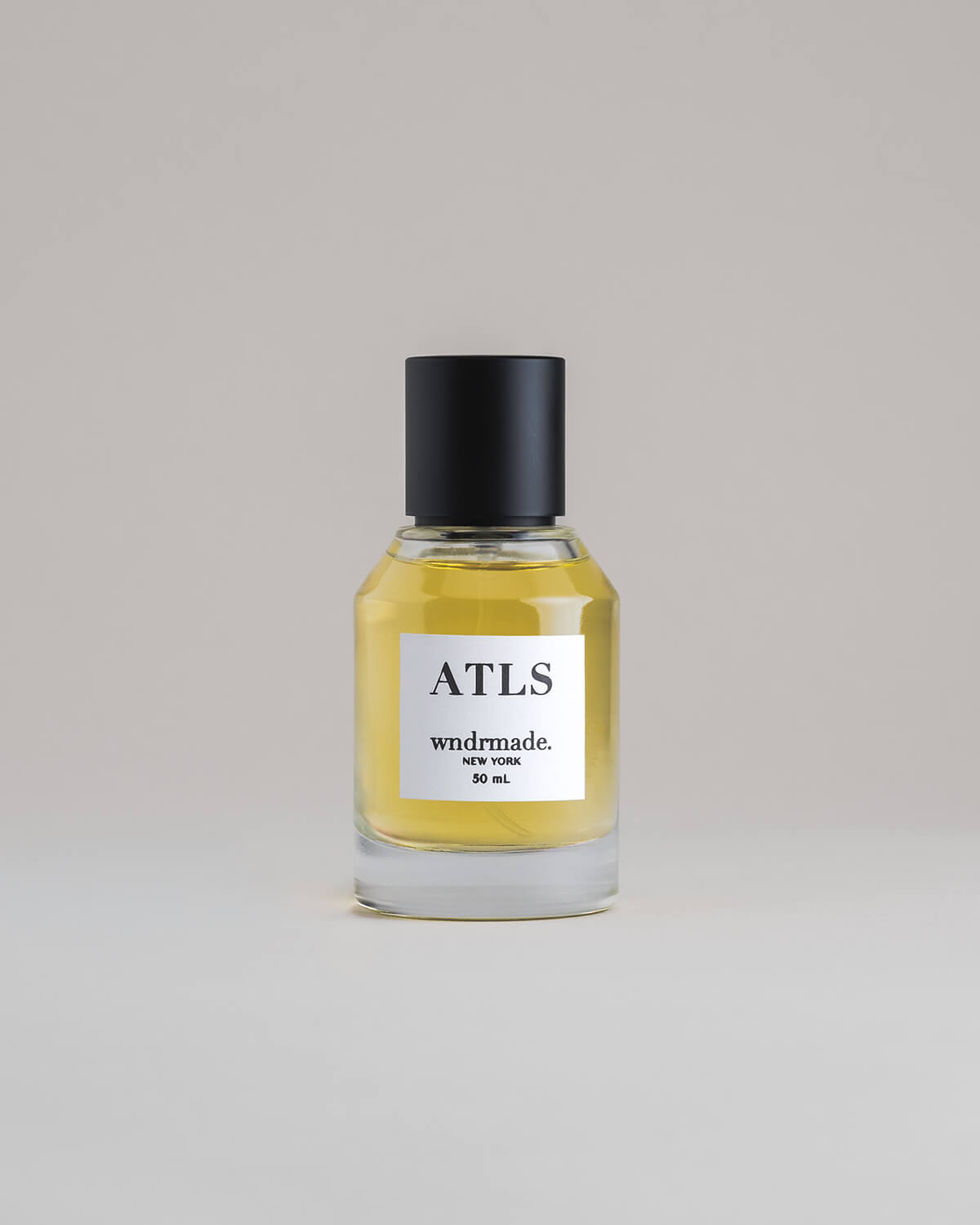 ATLS Atlas 50 mL botanical perfume in a minimalist glass bottle with a matte black cap and golden hue, set against a pale gray backdrop.