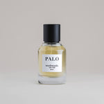 PALO Palo Santo 50 mL botanical perfume in a minimalist glass bottle with a matte black cap and light golden hue, set against a pale gray backdrop.