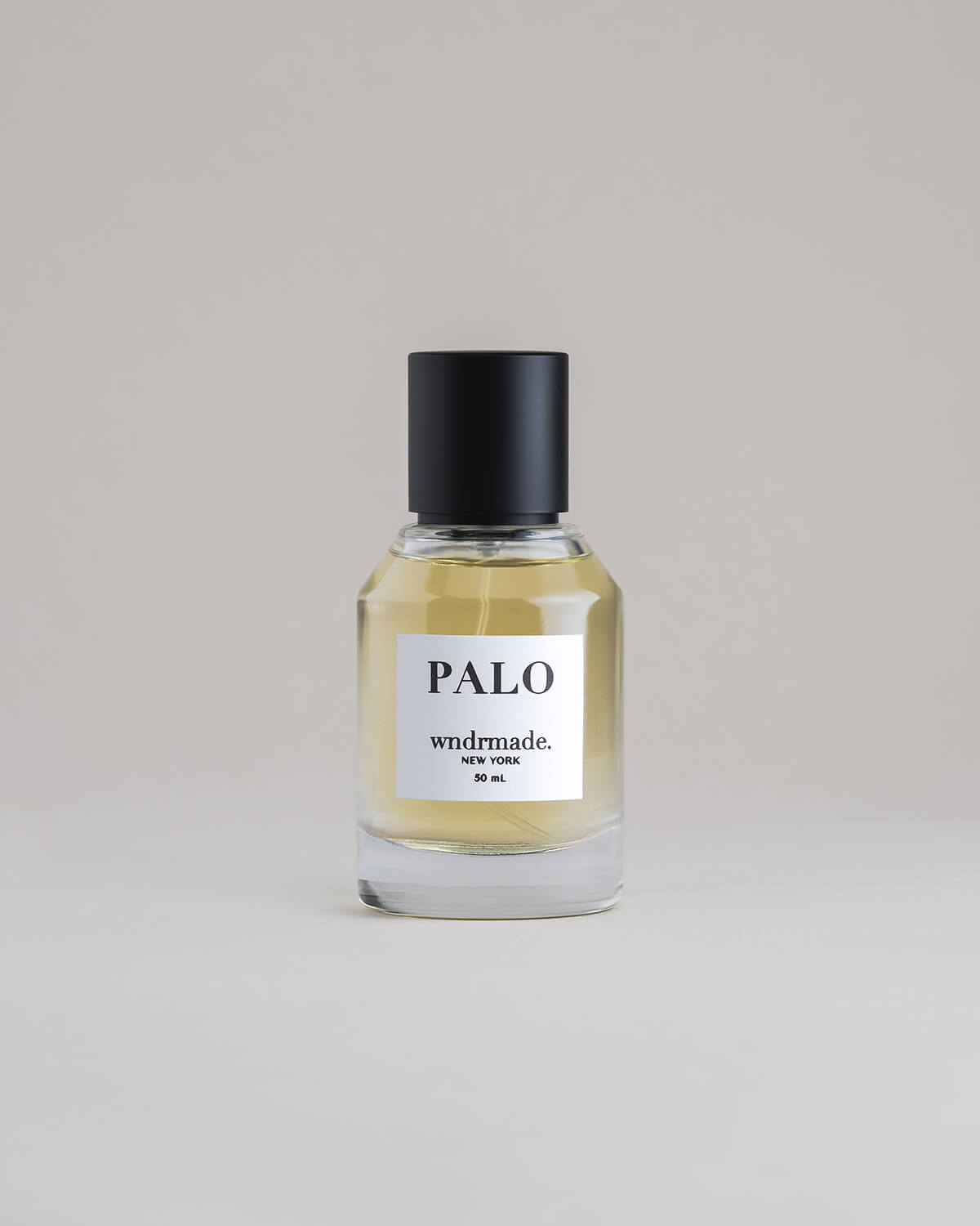 PALO Palo Santo 50 mL botanical perfume in a minimalist glass bottle with a matte black cap and light golden hue, set against a pale gray backdrop.