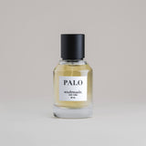 PALO Palo Santo 50 mL botanical perfume in a minimalist glass bottle with a matte black cap and light golden hue, set against a pale gray backdrop.