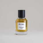 PCHL Patchouli 50 mL botanical perfume in a minimalist glass bottle with a matte black cap and a dark golden hue, set against a pale gray backdrop.