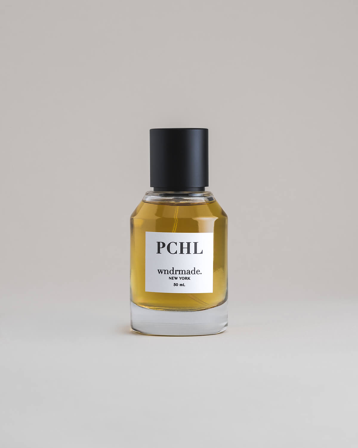 PCHL Patchouli 50 mL botanical perfume in a minimalist glass bottle with a matte black cap and a dark golden hue, set against a pale gray backdrop.