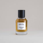 SNTL Sandalwood 50 mL botanical perfume in a minimalist glass bottle with a matte black cap and a dark golden hue, set against a pale gray backdrop.