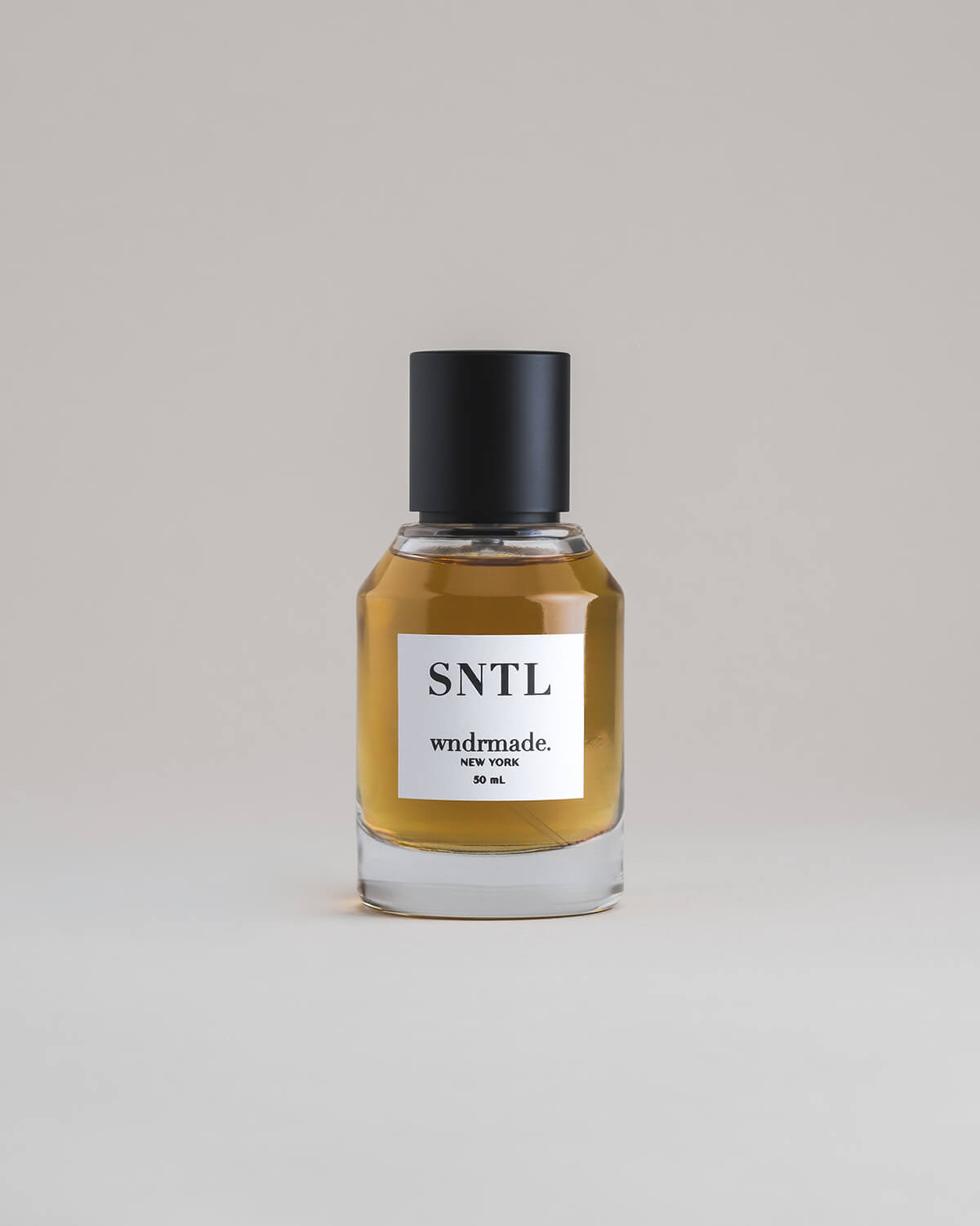 SNTL Sandalwood 50 mL botanical perfume in a minimalist glass bottle with a matte black cap and a dark golden hue, set against a pale gray backdrop.