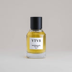 VTVR Vetiver 50 mL botanical perfume in a minimalist glass bottle with a matte black cap and golden hue, set against a pale gray backdrop.