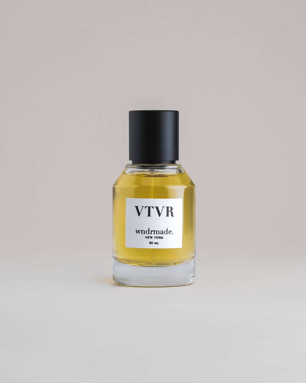 VTVR Vetiver 50 mL botanical perfume in a minimalist glass bottle with a matte black cap and golden hue, set against a pale gray backdrop.
