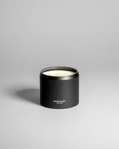 Wndrmade Hinoki candle in a black tin without lid on a neutral surface.
