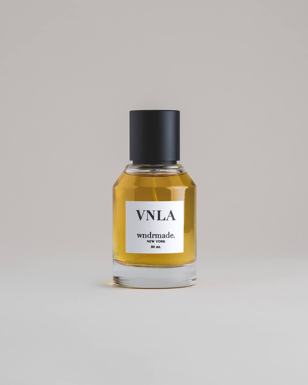 VNLA Vanilla 50 mL botanical perfume in a minimalist glass bottle with a matte black cap and golden hue, set against a pale gray backdrop.