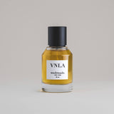 VNLA Vanilla 50 mL botanical perfume in a minimalist glass bottle with a matte black cap and golden hue, set against a pale gray backdrop.